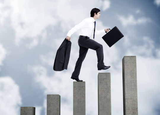 Young businessman climbing grey steps on sky background