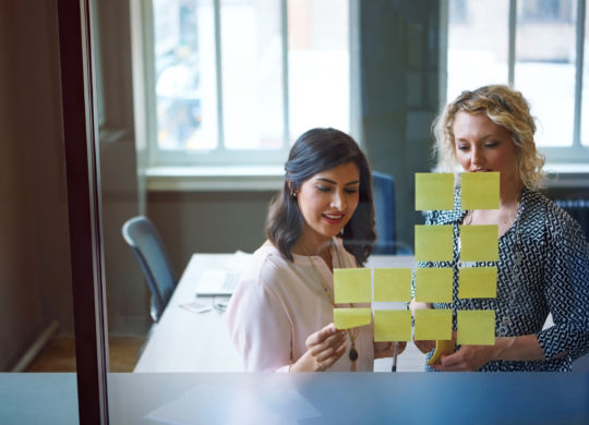 Shot of two businesswomen brainstorming with adhesive notes on a glass wall in an office