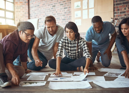 Shot of a team of entrepreneurs collaborating and sitting on the floor in a modern office